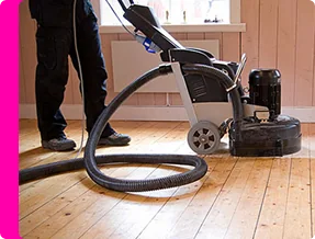 Sanding wood floor with vacuum-equipped machine.